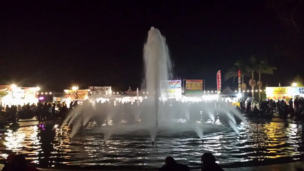 Lit-up fountain at night with crowds and food booths behind it at December Nights Balboa Park