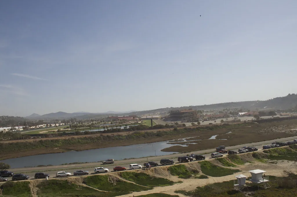 View across the San Dieguito Lagoon to the Del Mar racetrack grandstand, with cars parked along the coast road